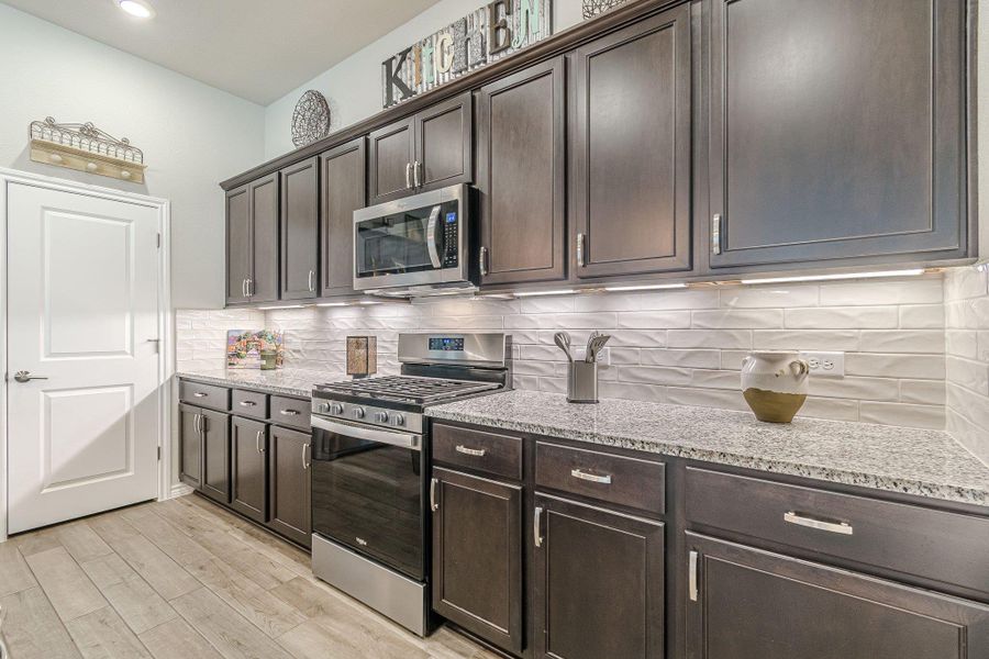 Kitchen with appliances with stainless steel finishes, dark brown cabinetry, light stone counters, and recessed lighting