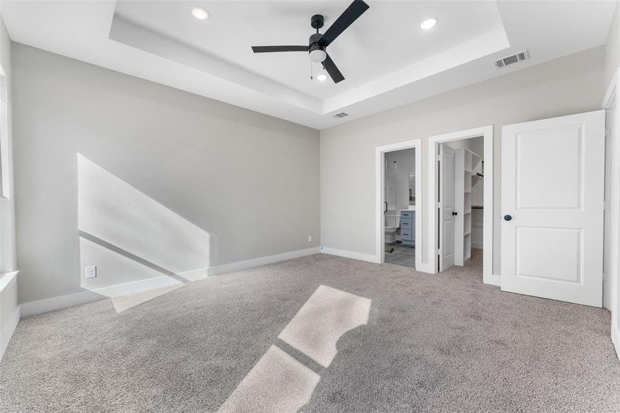 Unfurnished bedroom featuring a raised ceiling, ceiling fan, a walk in closet, and ensuite bath