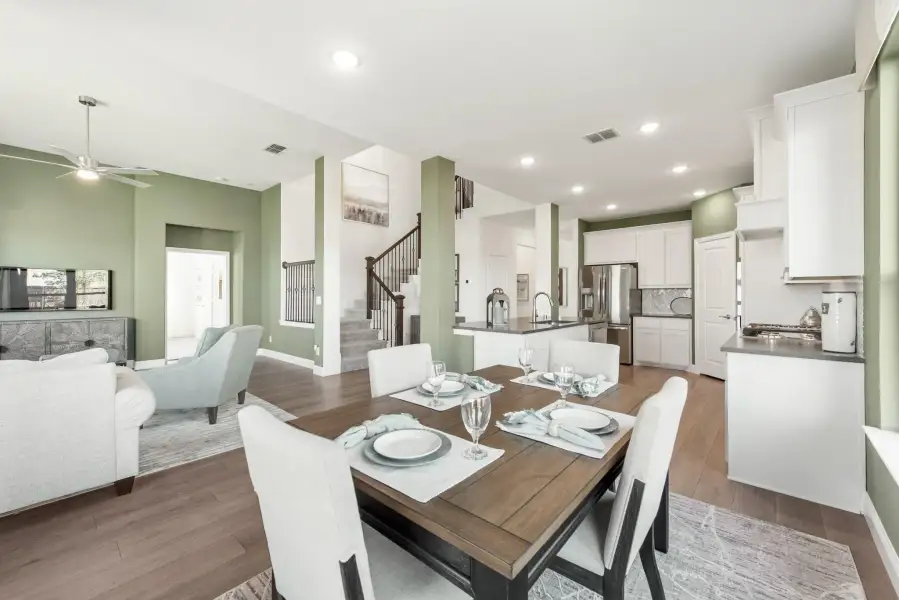 Open-concept dining area with wood table, white chairs, and kitchen and living room visible in background