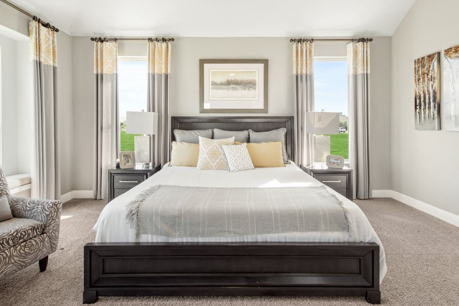 Bedroom with dark wood king bed, gray carpet, two windows with patterned curtains, and matching nightstands