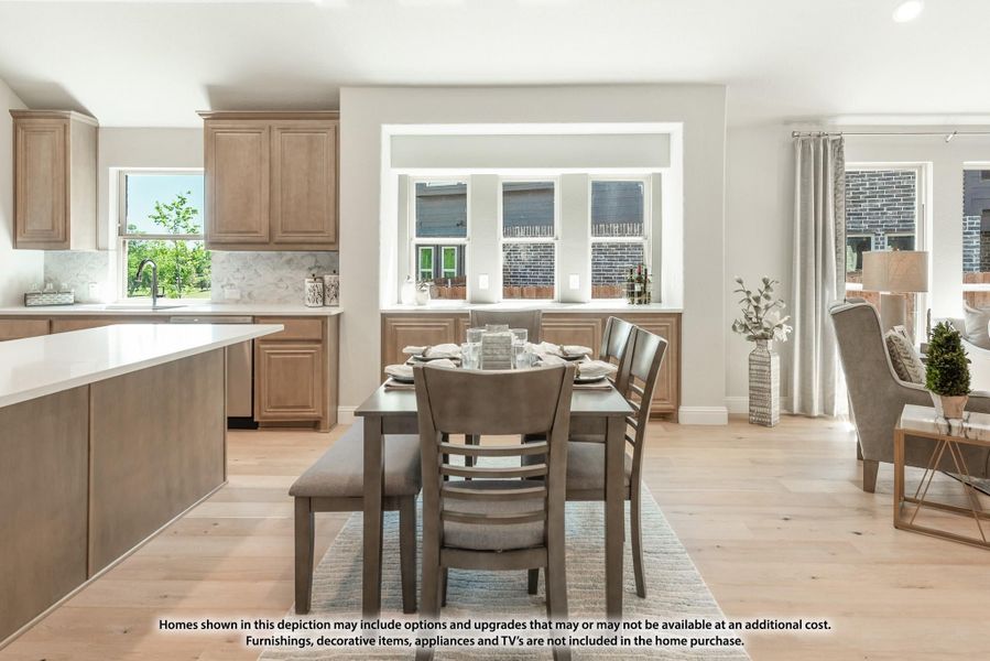 Open-concept dining area with gray table and bench, adjacent to kitchen with tan cabinets and light hardwood floors Open-concept dining area with gray table and bench, adjacent to kitchen with tan cabinets and light hardwood floors