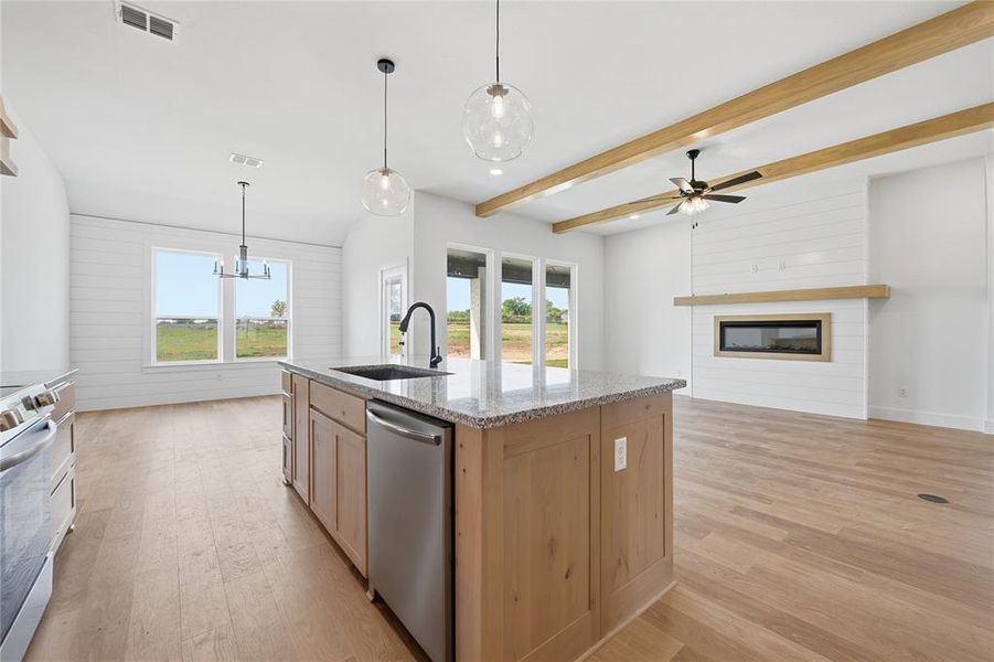 Kitchen with light wood finish cabinetry, light stone counters, stainless steel appliances, a kitchen island with sink, and beam ceiling Kitchen with light wood finish cabinetry, light stone counters, stainless steel appliances, a kitchen island with sink, and beam ceiling