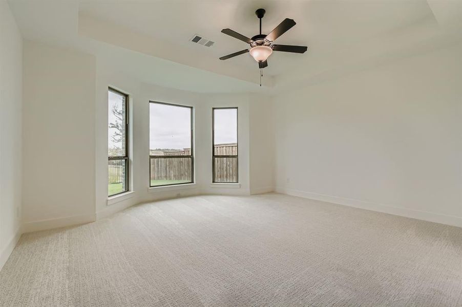 Empty room with a raised ceiling, light colored carpet, and a ceiling fan Empty room with a raised ceiling, light colored carpet, and a ceiling fan