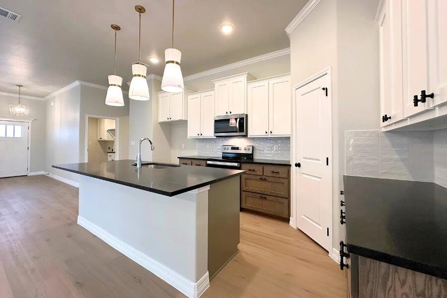 Kitchen with crown molding, white cabinets, an island with sink, light wood-type flooring, and stainless steel appliances