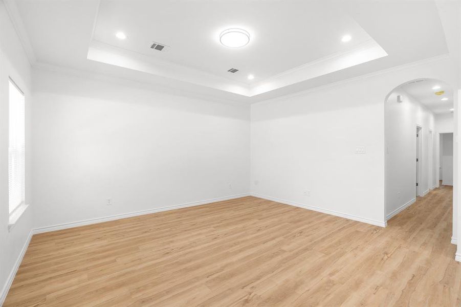 Spare room with a tray ceiling, arched walkways, light wood-style floors, crown molding, and recessed lighting Spare room with a tray ceiling, arched walkways, light wood-style floors, crown molding, and recessed lighting