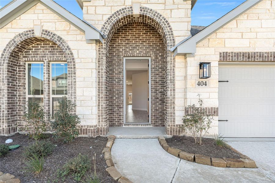Home exterior with brick and stone facade, arched entryway, open front door, and attached garage