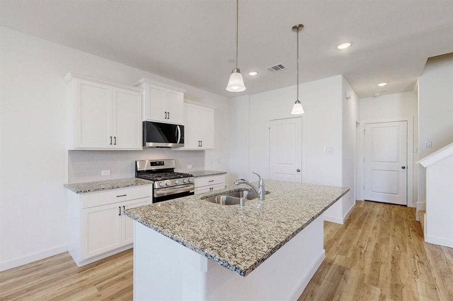 Kitchen featuring appliances with stainless steel finishes, white cabinetry, light stone countertops, light wood-style floors, and recessed lighting