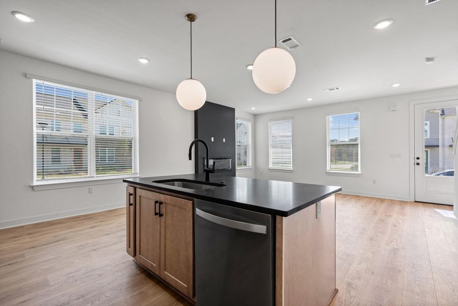 Kitchen island with dark countertop and integrated sink, pendant lighting, wood-finish flooring, and recessed ceiling lights