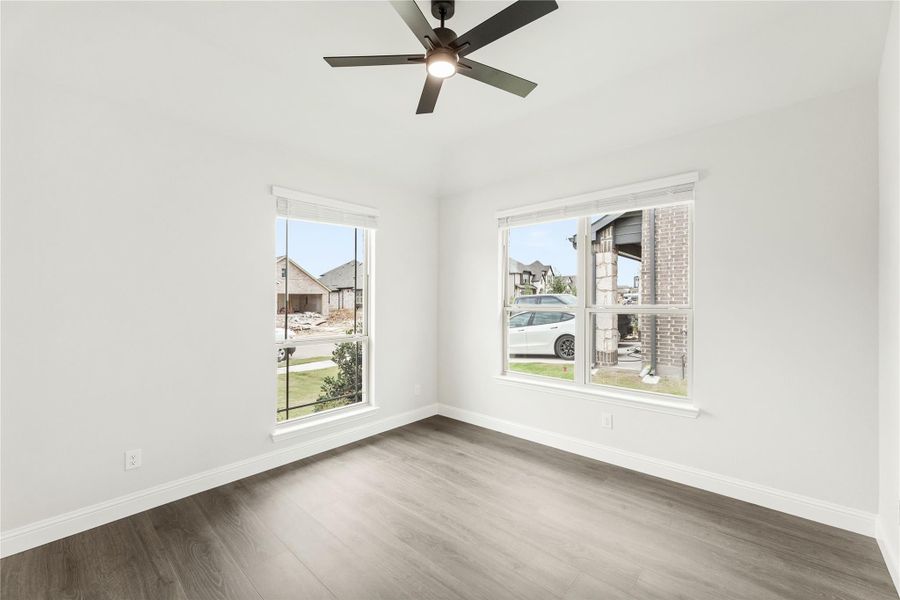 Empty bedroom with wood-look floors, ceiling fan, and two windows overlooking a neighborhood street Empty bedroom with wood-look floors, ceiling fan, and two windows overlooking a neighborhood street