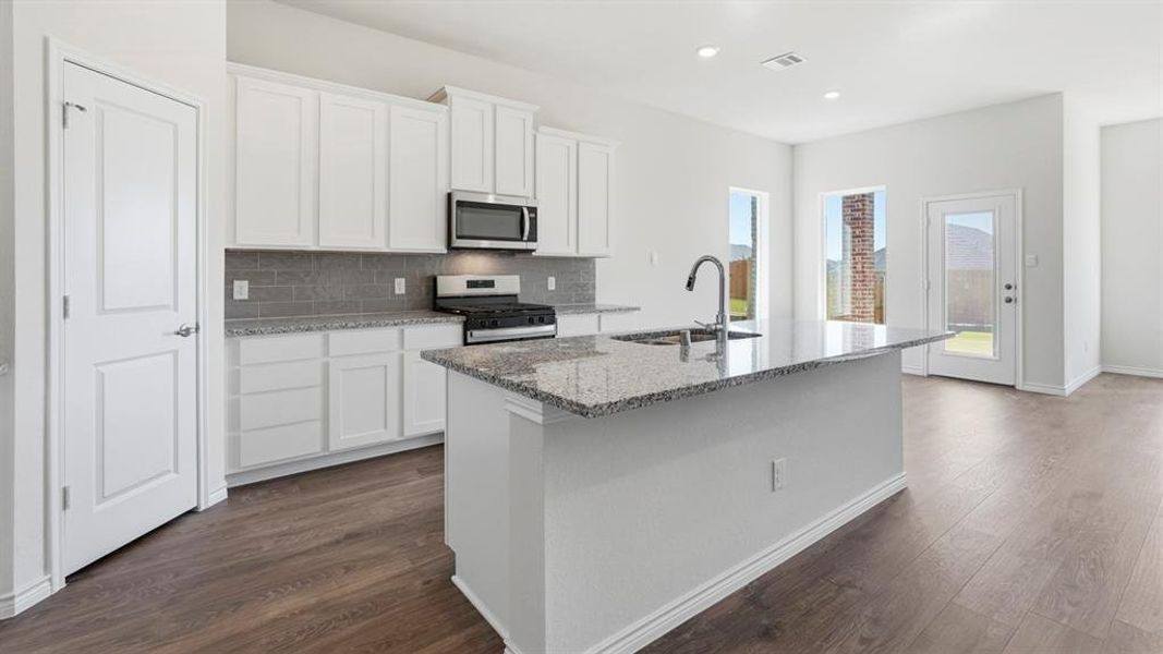Kitchen with decorative backsplash, light stone counters, white cabinets, appliances with stainless steel finishes, and an island with sink Kitchen with decorative backsplash, light stone counters, white cabinets, appliances with stainless steel finishes, and an island with sink