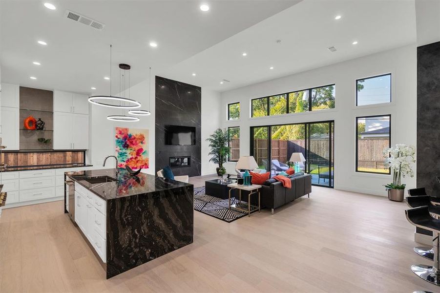 Kitchen featuring an island with sink, white cabinets, light hardwood / wood-style floors, a towering ceiling, and decorative light fixtures