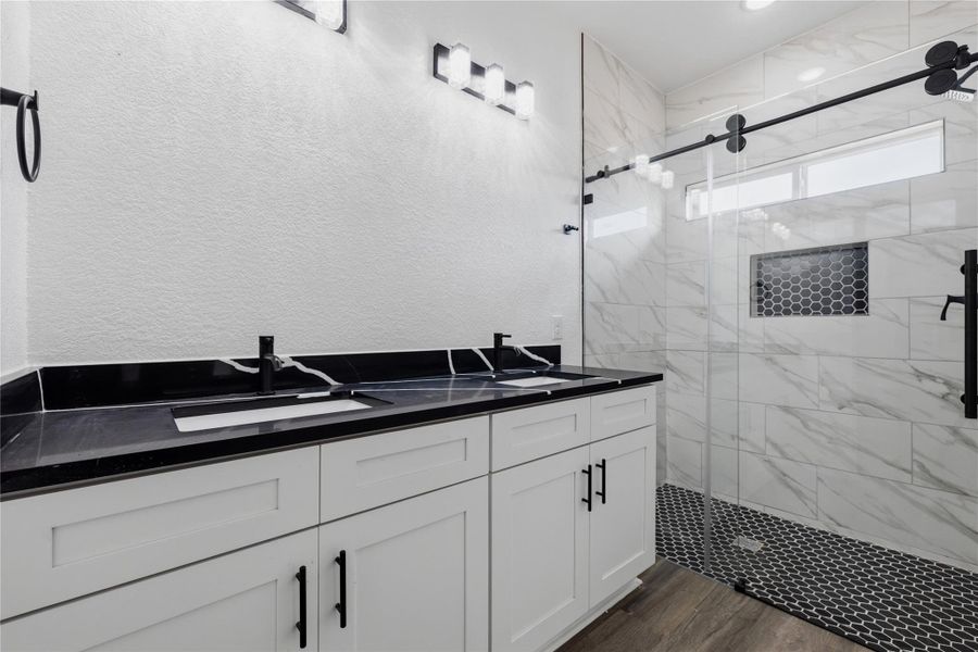 Primary bath with double vanity and a marble finish shower with all glass door