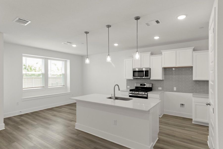 Kitchen with backsplash, white cabinetry, appliances with stainless steel finishes, an island with sink, and pendant lighting