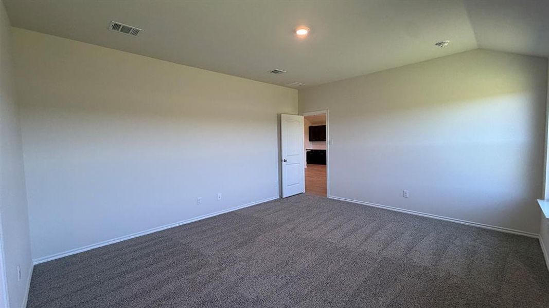 Spacious room featuring vaulted ceilings, light neutral wall paint, and gray textured carpeting
