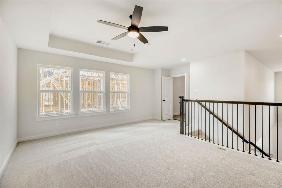 Carpeted empty room featuring ceiling fan and a tray ceiling