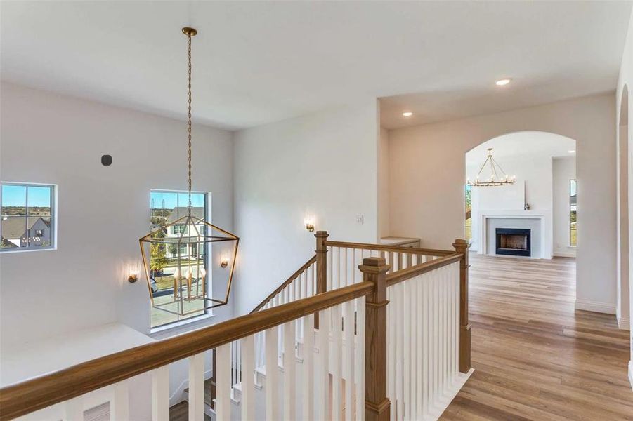 Hall with a chandelier, recessed lighting, light wood-type flooring, arched walkways, and an upstairs landing
