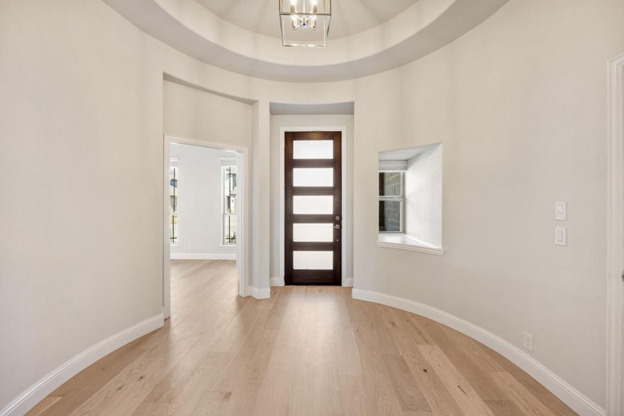 Round foyer with domed ceiling, chandelier, dark wood front door with glass panels, and light hardwood floors Round foyer with domed ceiling, chandelier, dark wood front door with glass panels, and light hardwood floors