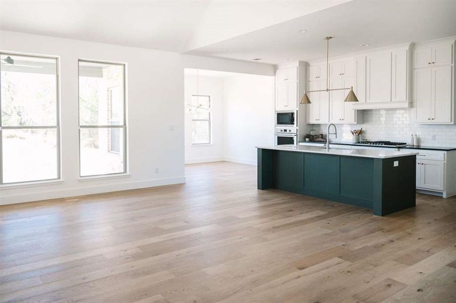 Kitchen with stainless steel appliances, white cabinets, light hardwood / wood-style floors, hanging light fixtures, and an island with sink