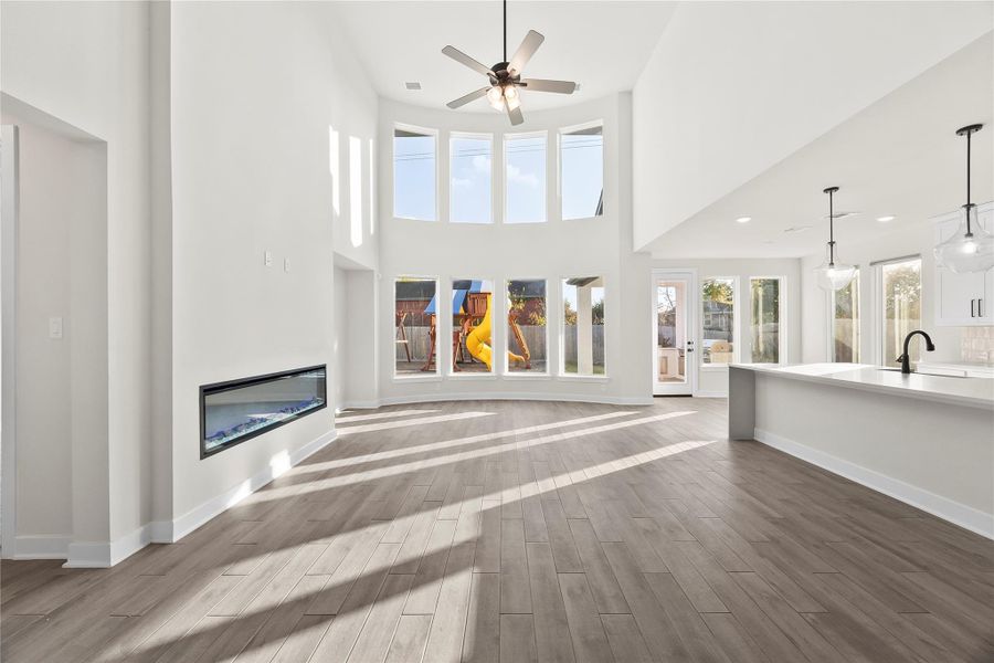 This bright, open-concept living space features high ceilings, a modern fireplace, large windows, and a seamless flow into a spacious kitchen with an island and pendant lighting. Perfect for family gatherings and entertaining. This bright, open-concept living space features high ceilings, a modern fireplace, large windows, and a seamless flow into a spacious kitchen with an island and pendant lighting. Perfect for family gatherings and entertaining.