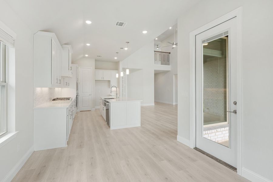 Open kitchen with white cabinets, center island, pendant lights, and light wood floors leading to living area