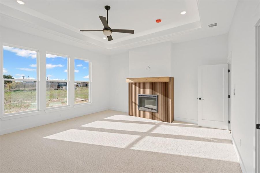 Unfurnished living room with a raised ceiling, ceiling fan, and light colored carpet