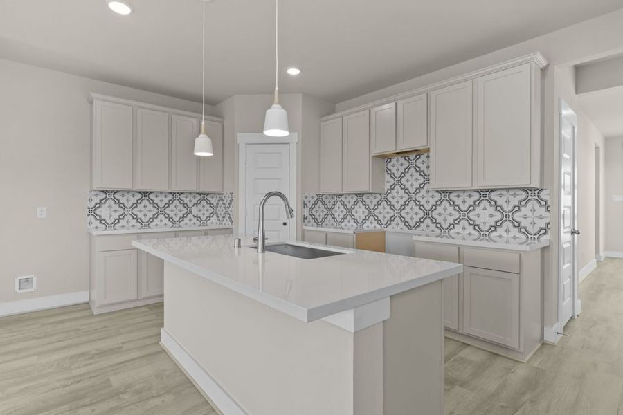Image of a kitchen with a designed backsplash, beige cabinets, a center island and white countertops