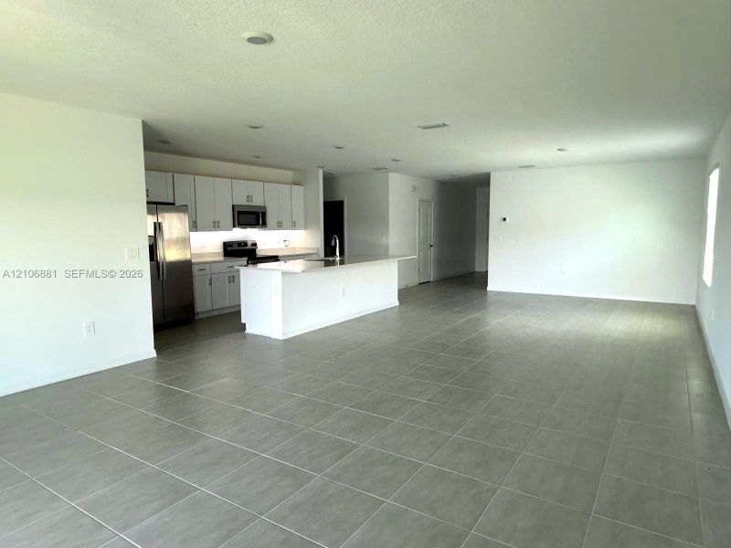 Open-concept space featuring large-format tile flooring, recessed lighting, and a kitchen equipped with white cabinetry, a stone-surface island, and stainless steel appliances