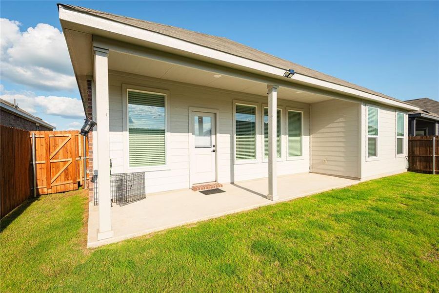 Rear elevation featuring a covered patio, multiple windows with blinds, a side entry door, and a privacy fence Rear elevation featuring a covered patio, multiple windows with blinds, a side entry door, and a privacy fence
