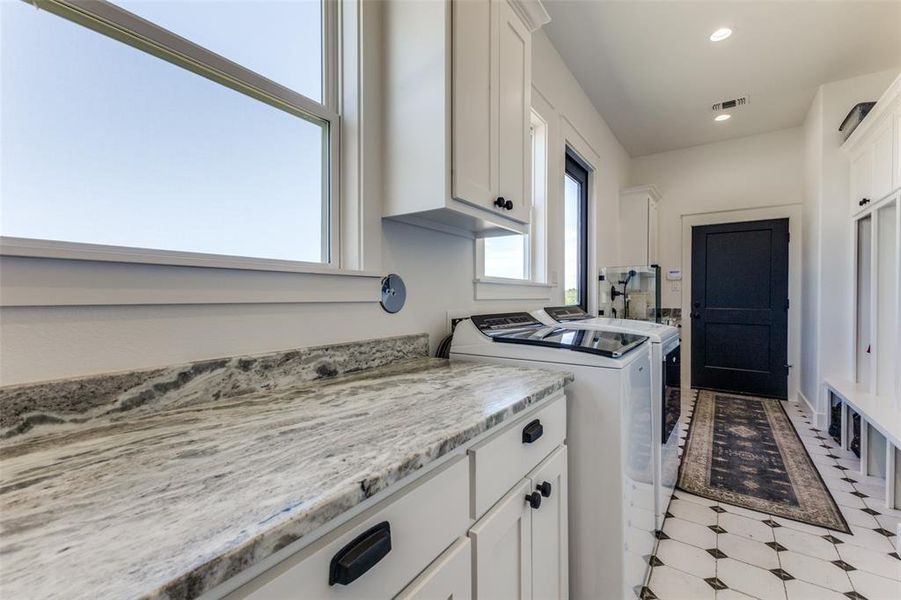 Kitchen featuring independent washer and dryer, white cabinets, light tile flooring, and light stone countertops Kitchen featuring independent washer and dryer, white cabinets, light tile flooring, and light stone countertops