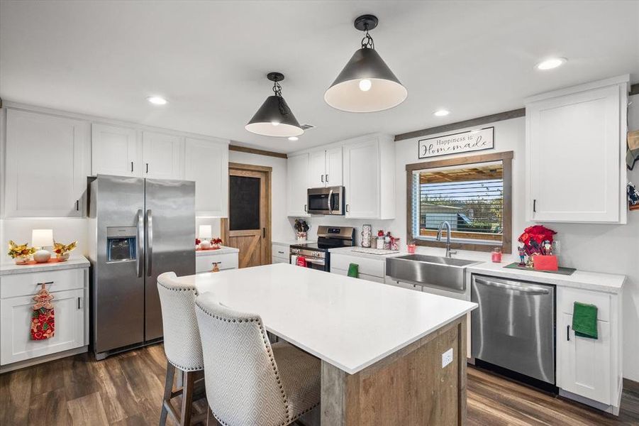 Spacious kitchen featuring an expansive central island with seating, stainless steel appliances, recessed lighting, and wood-finish flooring