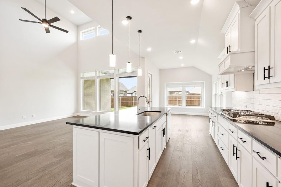 Open kitchen with white cabinets, dark countertops, center island with sink, and vaulted ceiling with pendant lights Open kitchen with white cabinets, dark countertops, center island with sink, and vaulted ceiling with pendant lights