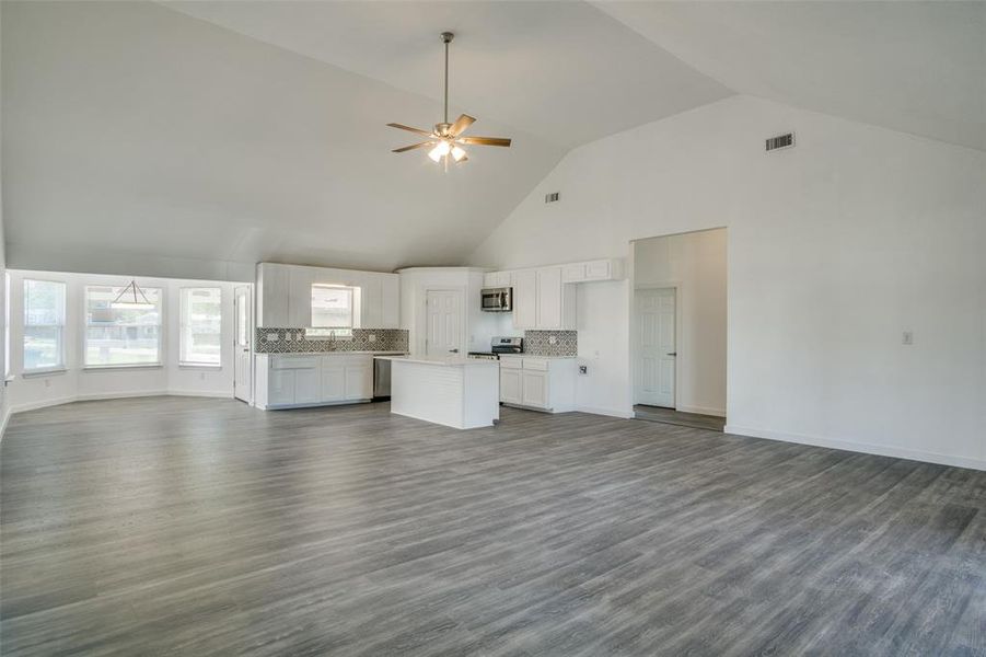 Unfurnished living room with high vaulted ceiling, dark wood-type flooring, and ceiling fan Unfurnished living room with high vaulted ceiling, dark wood-type flooring, and ceiling fan