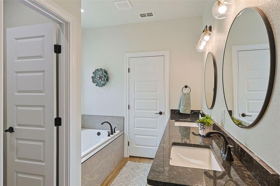 Dual vanity with dark granite countertops and undermount sinks, illuminated by a three-light fixture