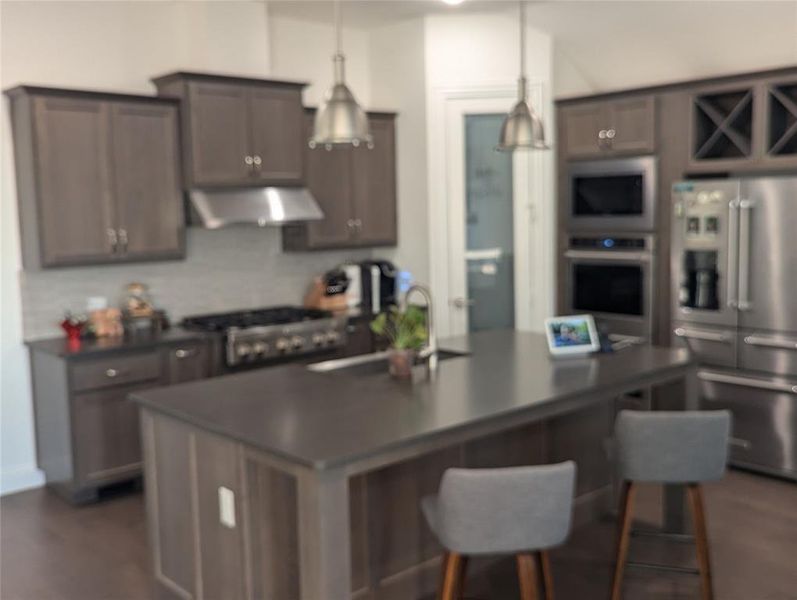 Kitchen featuring an island with sink,  stainless steel appliances, and pendant lighting