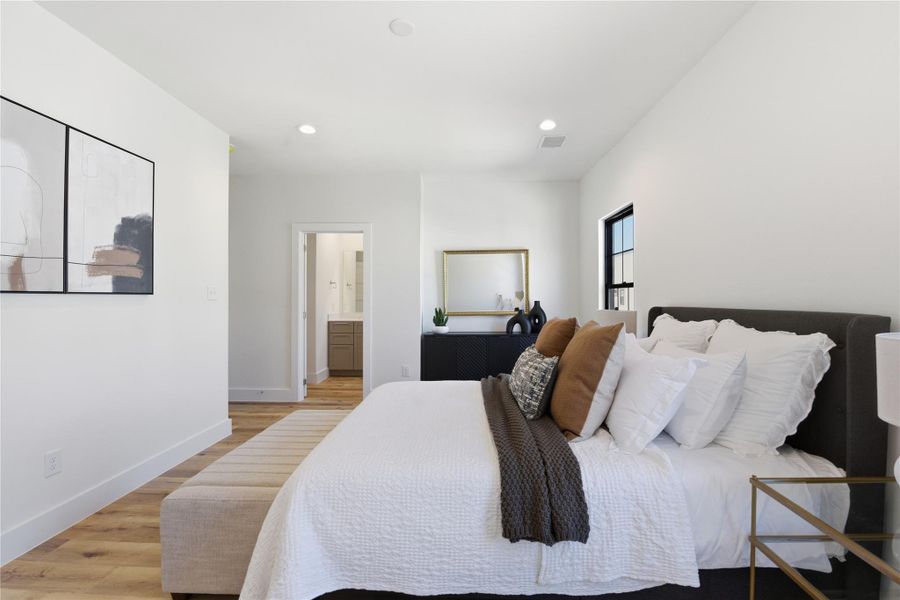 A bright bedroom with a comfortable bed, hardwood floors, modern décor, natural light from a window, and an ensuite bathroom for added convenience and privacy.