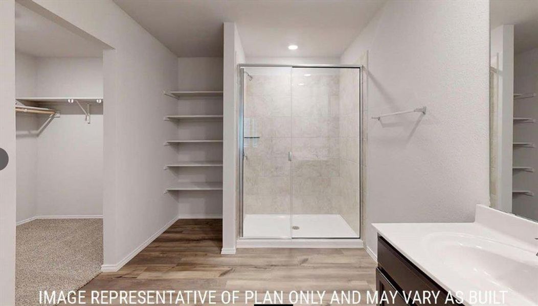Spacious bathroom featuring a glass-enclosed shower with tiled surround, wood-finish flooring, built-in shelving, and a vanity with an integrated sink Spacious bathroom featuring a glass-enclosed shower with tiled surround, wood-finish flooring, built-in shelving, and a vanity with an integrated sink