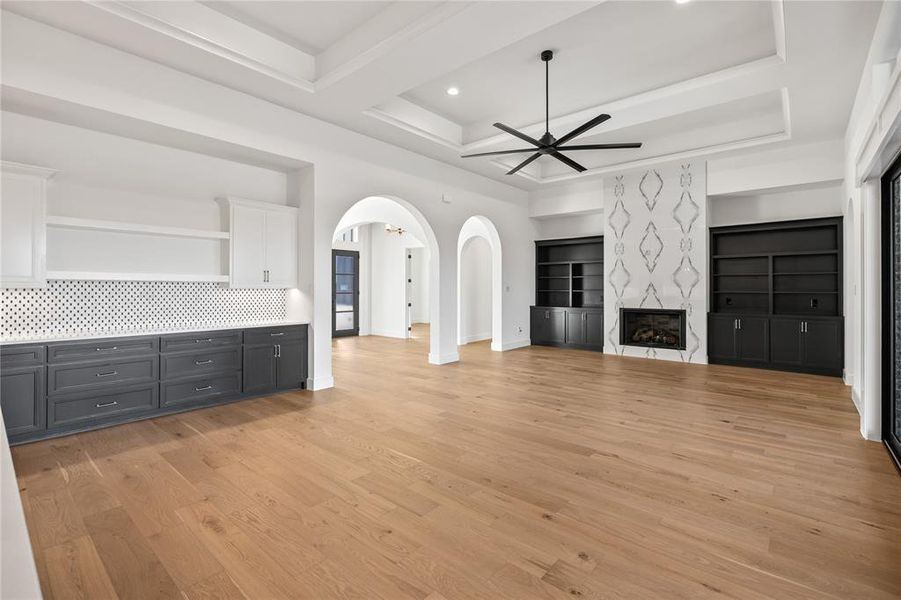 Unfurnished living room featuring ceiling fan, light wood-style floors, arched walkways, a fireplace, and a tray ceiling Unfurnished living room featuring ceiling fan, light wood-style floors, arched walkways, a fireplace, and a tray ceiling