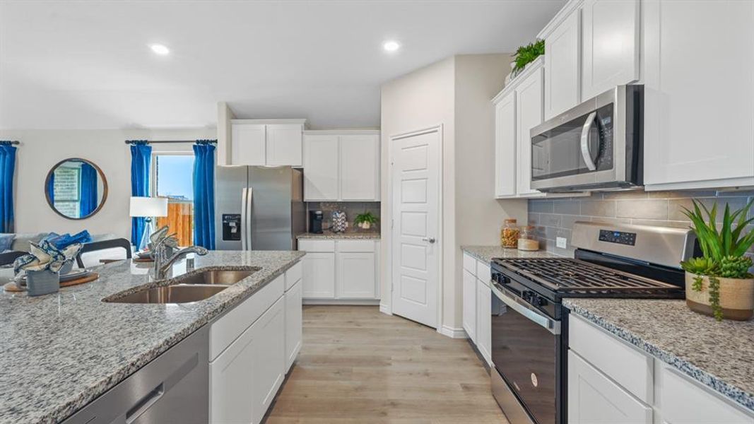 Kitchen with stainless steel appliances, light wood-style flooring, white cabinetry, decorative backsplash, and light stone counters Kitchen with stainless steel appliances, light wood-style flooring, white cabinetry, decorative backsplash, and light stone counters