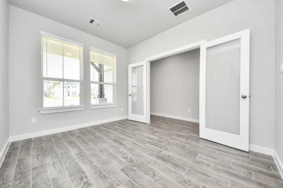 Experience the perfect blend of sophistication and warmth in this home office, boasting elegant wood-look tile flooring and flooded with natural light from expansive windows and French doors. Sample photo of completed home with similar floor plan. Actual colors and selections may vary. Experience the perfect blend of sophistication and warmth in this home office, boasting elegant wood-look tile flooring and flooded with natural light from expansive windows and French doors. Sample photo of completed home with similar floor plan. Actual colors and selections may vary.