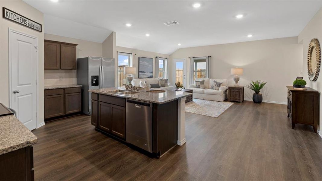 Kitchen featuring open floor plan, dark wood finish cabinetry, lofted ceiling, an island with sink, and stainless steel appliances