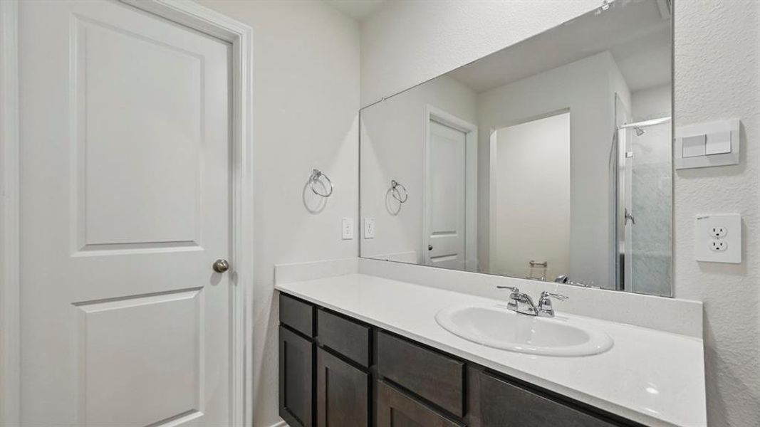 The bathroom features a vanity with dark wood cabinetry, a white countertop, and a large mirror