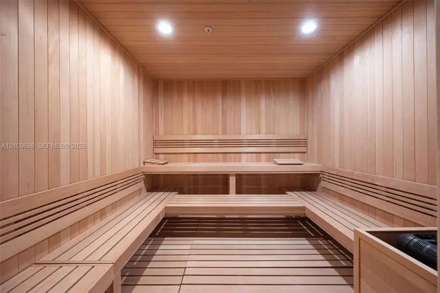 Sauna featuring natural wood-paneled walls, multi-level built-in bench seating, recessed lighting, and a slatted wood floor