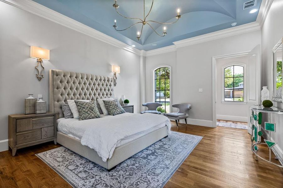 Bedroom featuring a raised ceiling, a high ceiling, hardwood / wood-style flooring, a notable chandelier, and crown molding