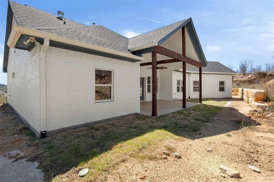 Back of property featuring brick siding, roof with shingles, a ceiling fan, and a patio area