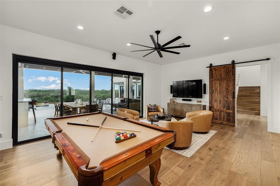 Playroom featuring ceiling fan, a barn door, light hardwood / wood-style floors, and billiards