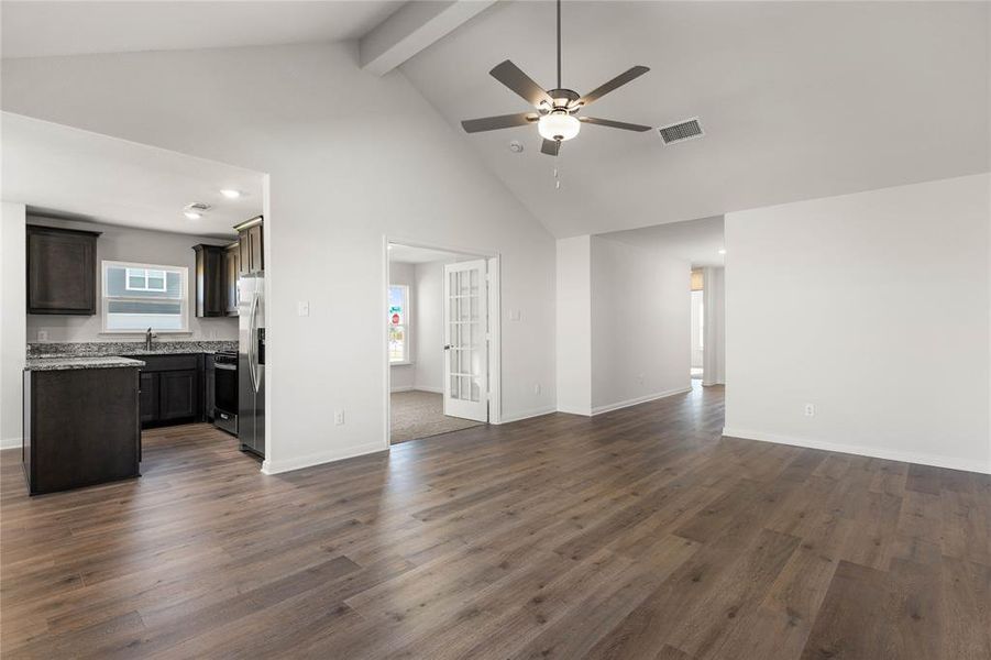 Unfurnished living room featuring high vaulted ceiling, beamed ceiling, dark wood-style floors, and a ceiling fan Unfurnished living room featuring high vaulted ceiling, beamed ceiling, dark wood-style floors, and a ceiling fan