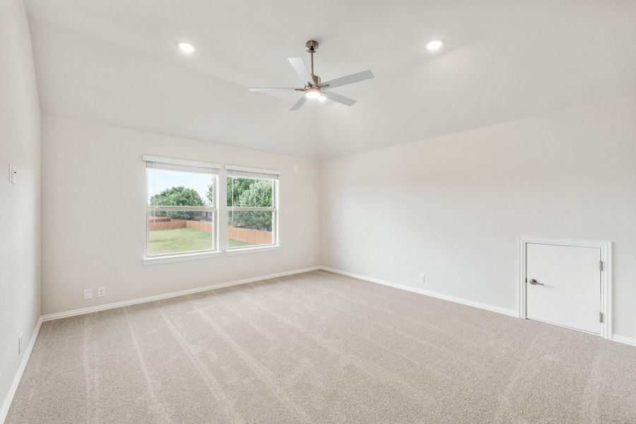Empty bedroom with vaulted ceiling, ceiling fan, carpet flooring, and two windows overlooking backyard