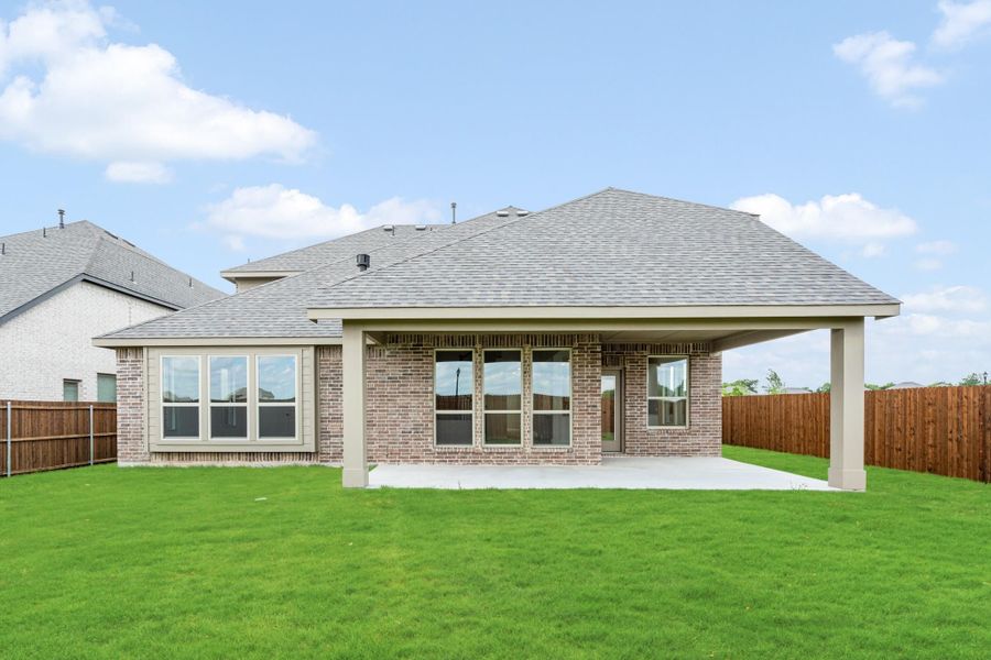 Rear view of single-story brick home with covered patio, concrete slab, and fenced backyard with green lawn Rear view of single-story brick home with covered patio, concrete slab, and fenced backyard with green lawn