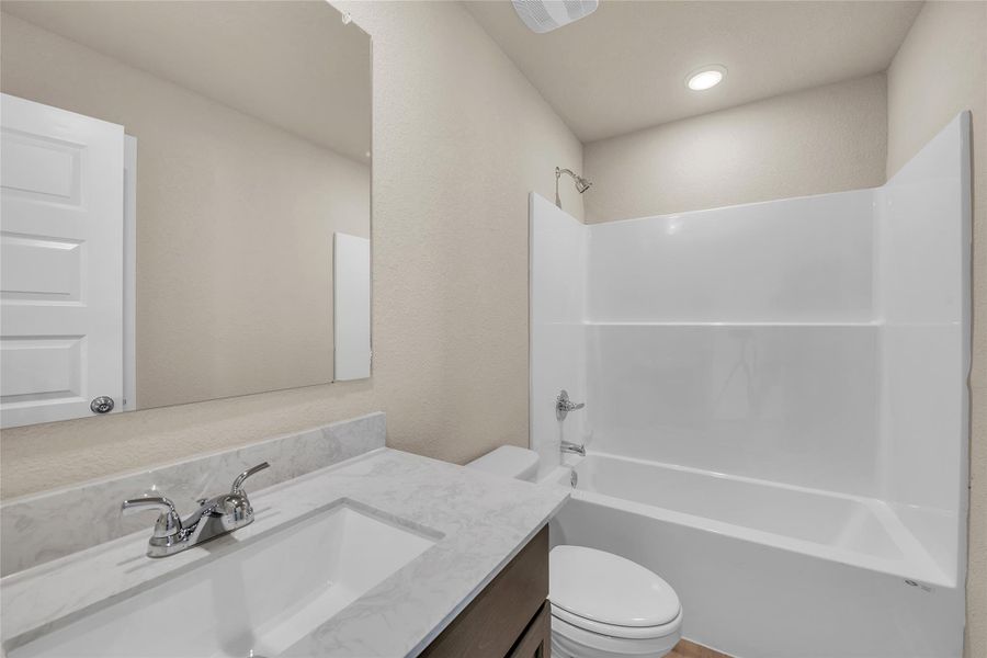 Bathroom with washtub / shower combination, vanity, and a textured wall