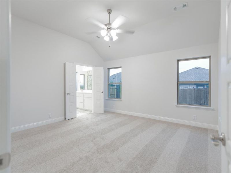 Unfurnished room featuring ceiling fan, light colored carpet, a healthy amount of sunlight, and vaulted ceiling